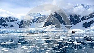 Beautiful scenery with leopard seal on ice floe and small zodiac with tourists in Paradise Bay, Antarctica