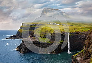 Beautiful scenery of the majestic Mulafossur Waterfall at evening. Stunning view of Vagar island, Faroe Islands, Denmark, Europe