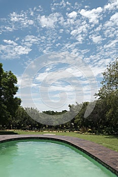 Beautiful scenery of a pool surrounded by beautiful green trees under the breathtaking cloudy sky