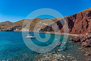 Beautiful scenery of red sand beach with a boat in Akrotiri village on Santorini