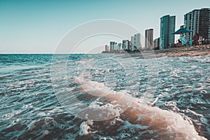 Beautiful scenery of the sea waves splashing on the beach in Ondas with buildings in the background photo