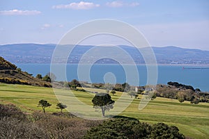 Beautiful scenic aerial-like bright view of golf course with trees, Irish sea, Dublin bay, Poolbeg lighthouse and Dublin Mountains