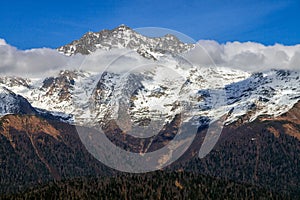 Beautiful scenic blue sky sunny autumn landscape of snowy Chugush mountain peak in Caucasus Nature Reserve in Krasnaya Polyana,