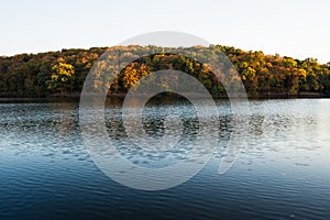 Beautiful scenic panoramic autumn view on bank of lake with trees. Golden hour.