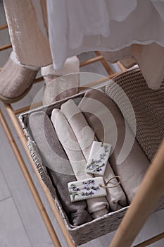 Beautiful scented wax sachets and folded clothes in wicker basket on rack indoors