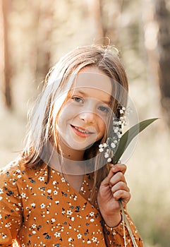 Beautiful school-age girl with lily of the valley flowers in her hand. Summer, sunset