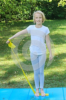 Beautiful school aged kid girl playing sports with a latex band and mat outdoors in the park