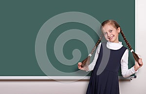 Beautiful school girl with pigtail smiled near blank chalkboard background, dressed in classic black suit, education concept