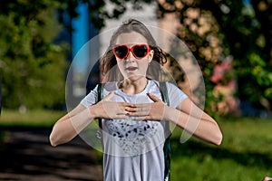 Beautiful schoolgirl girl. Summer nature after school. Glasses, heart is shaped. Smiles happily. Gestures of hands are