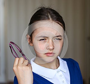 Beautiful schoolgirl in school uniform screwing up her eyes trying to see something without glasses