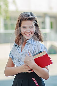 Beautiful schoolgirl teen holds textbooks. Pupil in front of school in schoolyard