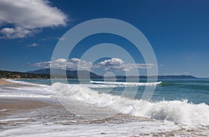 Beautiful sandy beach, sea waves, foam, blue sky, white clouds.