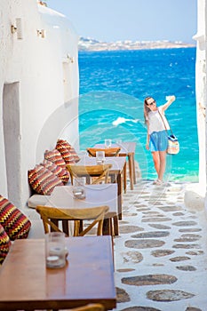 Beautiful sea view in outdoor cafe Mykonos on Cyclades islands. Young woman taking selfie with this amazing view