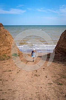 Beautiful seascape. The girl in a dress and a white hat goes down to the sea