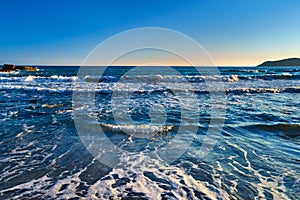 Beautiful seascape of low tidal waves, clear sunset sky, hazy hills. Clear blue and azure waters approaching with little