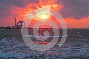 Beautiful seascape with red sunset, sea port with ships and storm waves in evening.