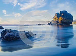 Beautiful seascape. A rock in the middle of the ocean and a lot of stones. Pure clear blue water. Blue sky and light white clouds