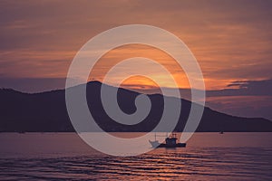 Beautiful seascape view of fishing boat floating on the sea with sunset light in the background at twilight time.