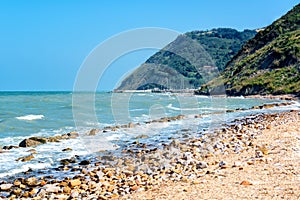 Beautiful seascape with view on sea and mountains on summer day, sea shore with pebble stones and cutwater. Adriatic
