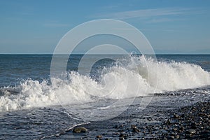 Beautiful seascape. Waves, pebble beach, sea spray, blue sea and blue sky.