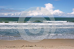 Beautiful seaside landscape with calm sea surf with waves runs to the empty sandy beach and white clouds on skyline in sunny day