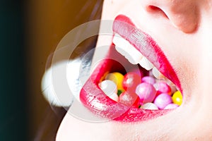 Beautiful seductive red lips and open mouth filled with colored balls closeup