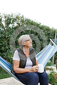 Beautiful senior blonde woman reading book and sitting in hammock in the garden