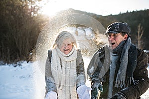 Beautiful senior couple blowing snow in sunny winter nature