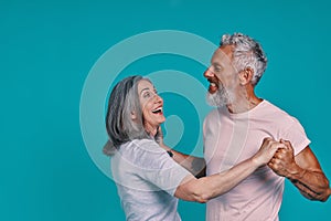 Beautiful senior couple dancing and smiling while standing together against blue background