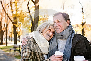 Beautiful senior couple hugging in park, drinking coffee. Autumn