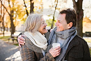 Beautiful senior couple hugging in park, drinking coffee. Autumn