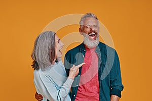 Beautiful senior couple laughing while standing together against orange background