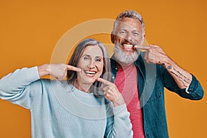 Beautiful senior couple looking at camera and pointing their teeth with smile