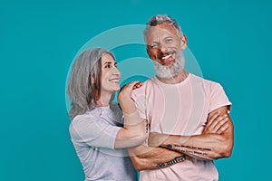 Beautiful senior couple looking at camera and smiling while standing together against blue background