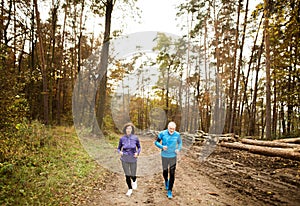 Beautiful senior couple running outside in sunny autumn forest