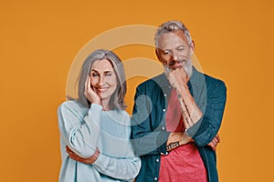 Beautiful senior couple smiling while standing together against orange background