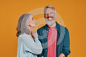 Beautiful senior couple smiling while standing together against orange background