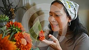 Beautiful senior female florist smelling orange flowers. Floristry, small business and lifestyle concept