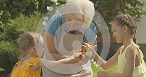 Beautiful senior grandmother holding baby duck as little sisters caressing duckling. Portrait of cheerful Caucasian