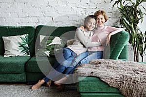 Beautiful senior mom and her adult daughter are hugging, looking at camera and smiling.