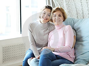 Beautiful senior mom and her adult daughter are hugging, looking at camera and smiling.