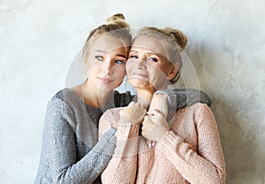 Beautiful senior mom and her adult daughter are hugging, looking at camera and smiling.