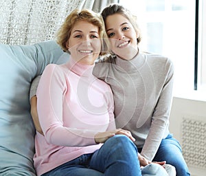 Beautiful senior mom and her adult daughter are hugging, looking at camera and smiling.