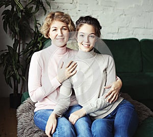 Beautiful senior mom and her adult daughter are hugging, looking at camera and smiling.