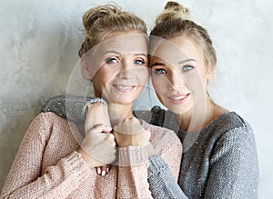 Beautiful senior mom and her adult daughter are hugging, looking at camera and smiling