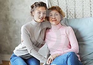 Beautiful senior mom and her adult daughter are hugging, looking at camera and smiling.