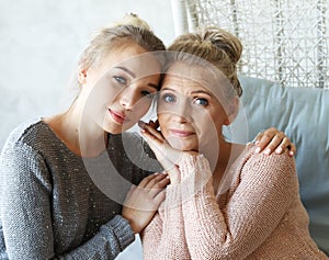 Beautiful senior mom and her adult daughter are hugging, looking at camera and smiling. At Home.