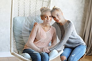 Beautiful senior mom and her adult daughter are hugging, looking at camera and smiling. At Home.
