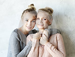 Beautiful senior mom and her adult daughter are hugging, looking at camera and smiling.