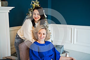 Beautiful senior mom and her adult daughter are smiling while watching a child playing at home with a christmas tree